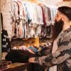 bearded-young-man-counter-looking-clothes-hanging-rail-min